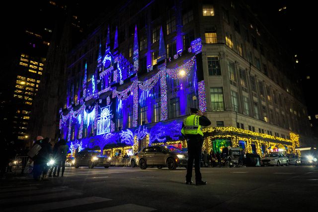 A photo of a cop in front of the lit up Saks Fifth Avenue store